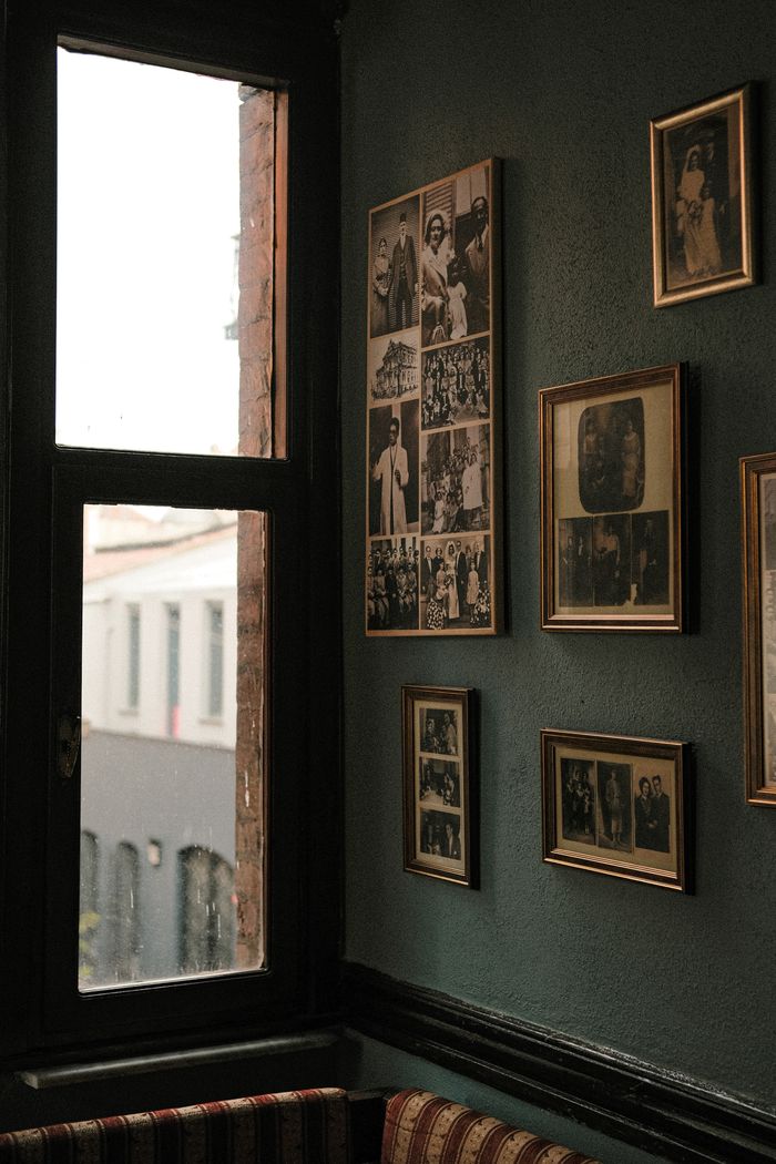 Home A collection of vintage photographs on a wall beside a window in a cozy, retro-style room.